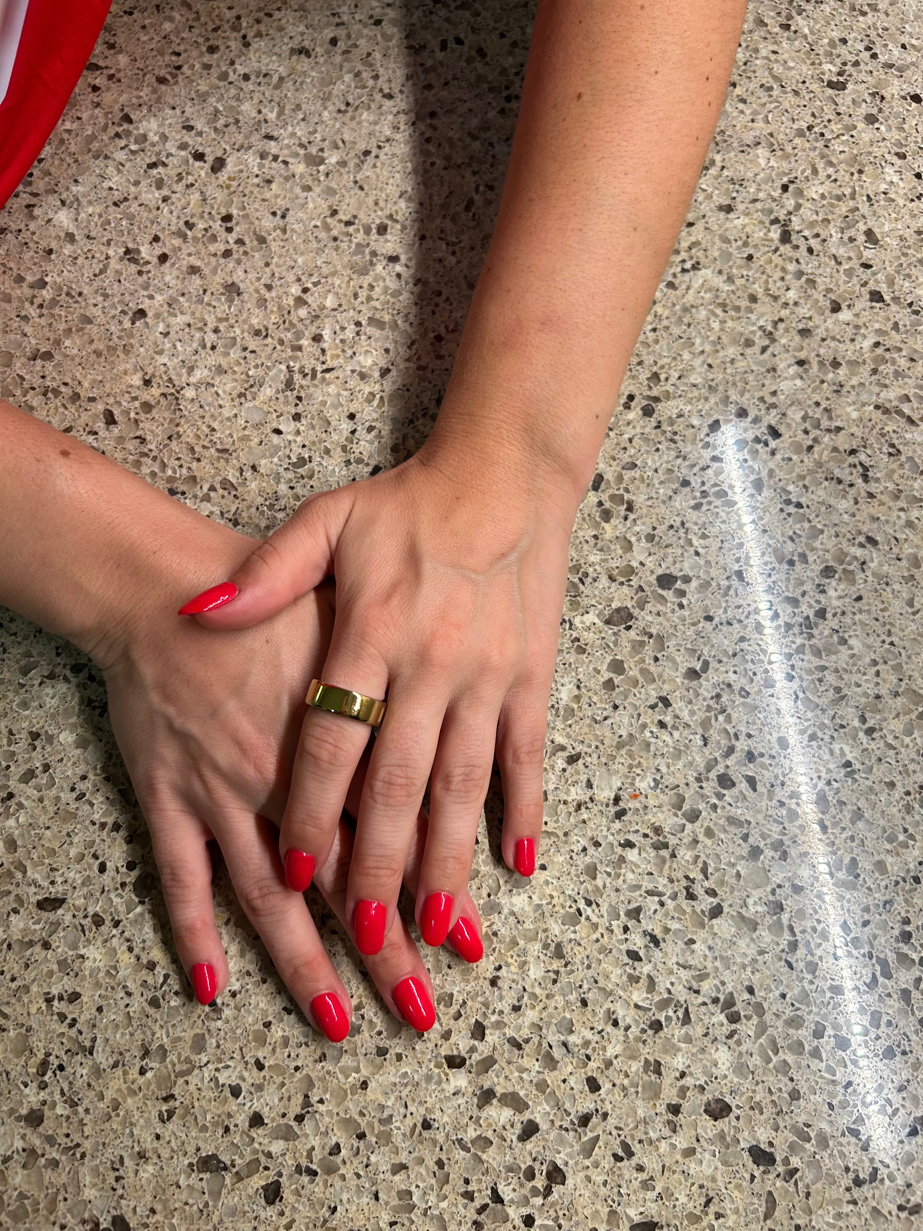 A close-up of two hands with glossy red gel-polished nails filed into a clean, rounded oval shape, resting on a stone countertop at the Roanoke studio.