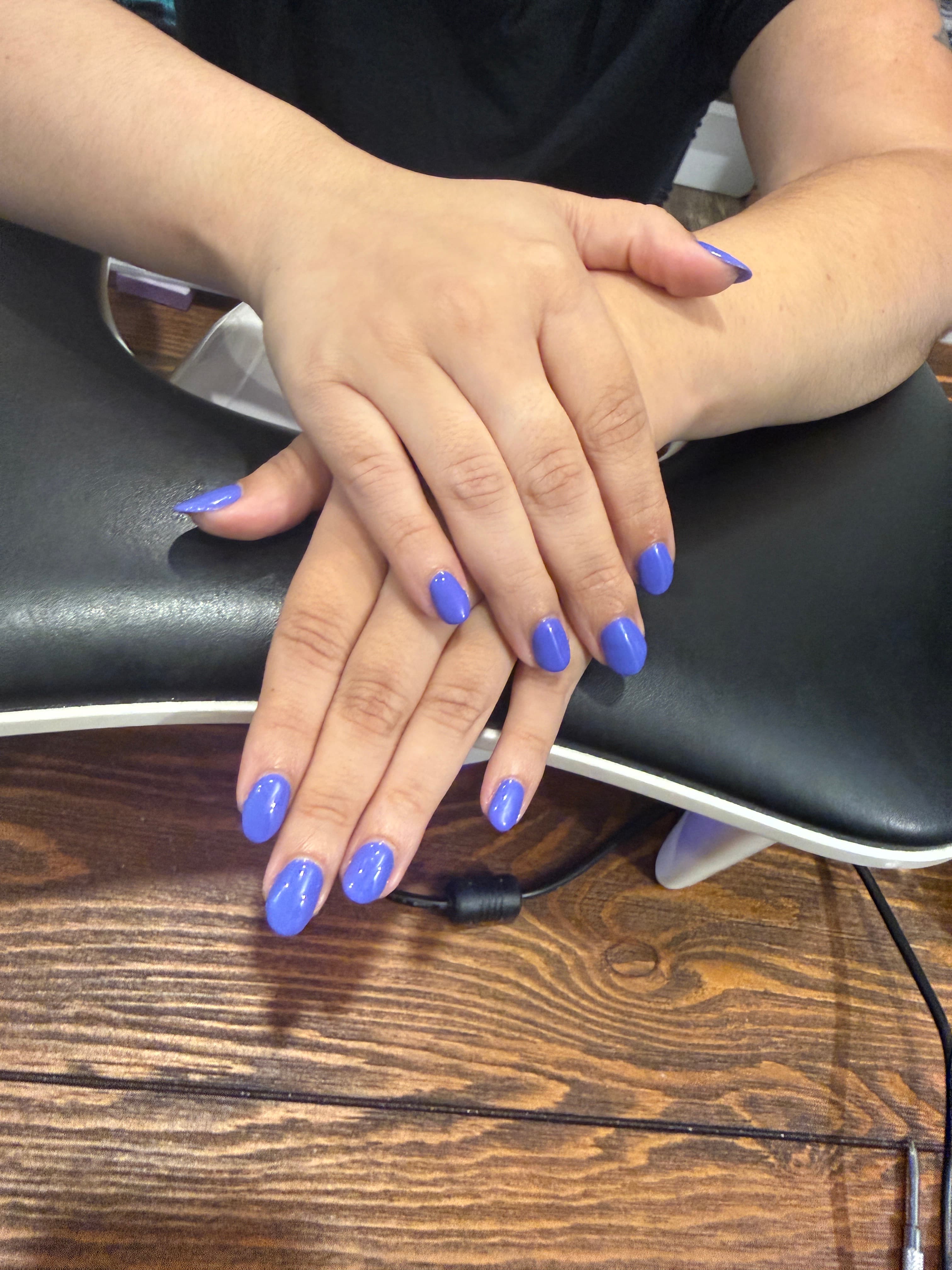 A glossy periwinkle gel manicure with a clean, rounded oval shape, one hand resting over the other.