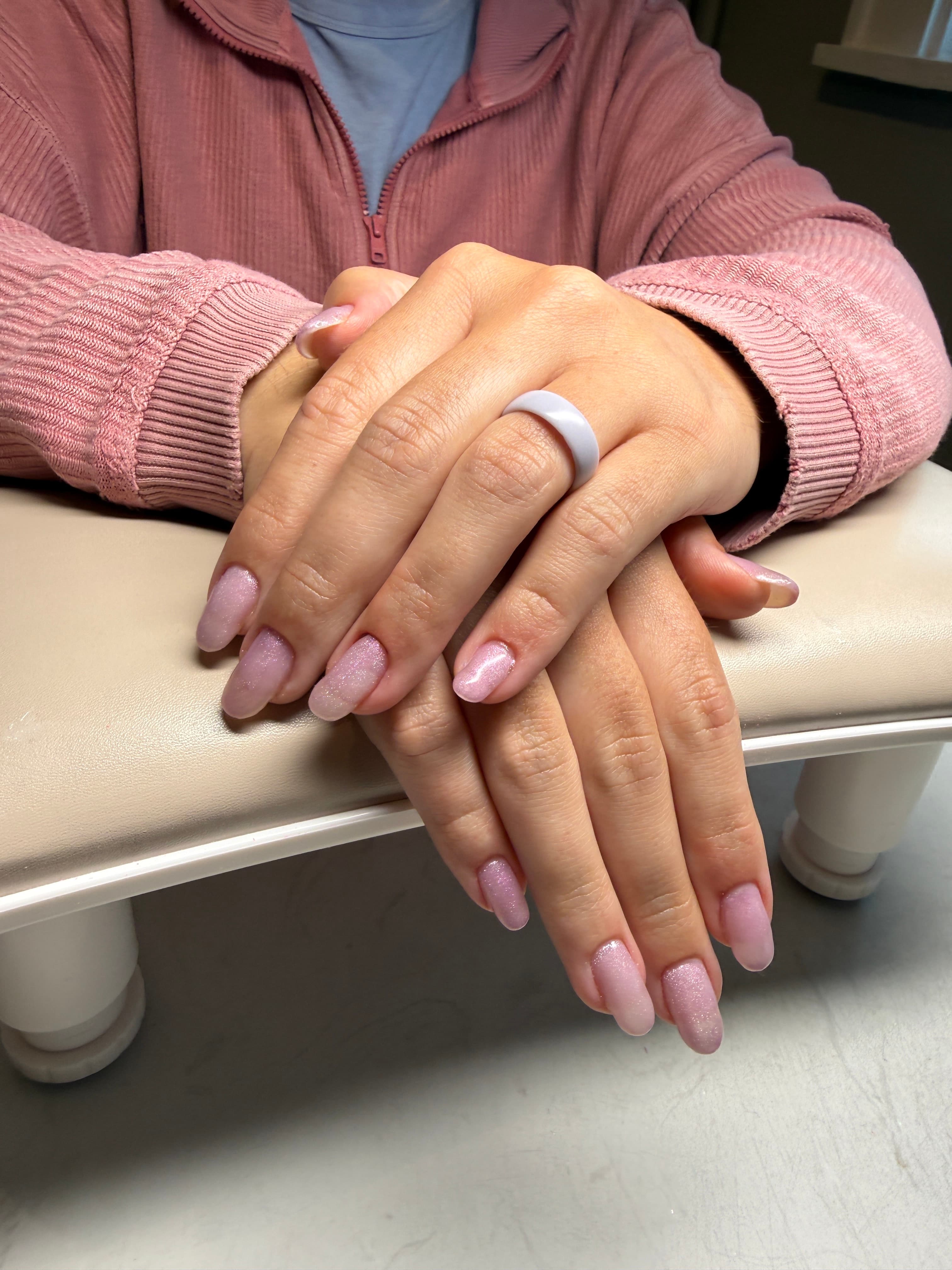 A close-up of a hand with pink nails in a manicure chair.